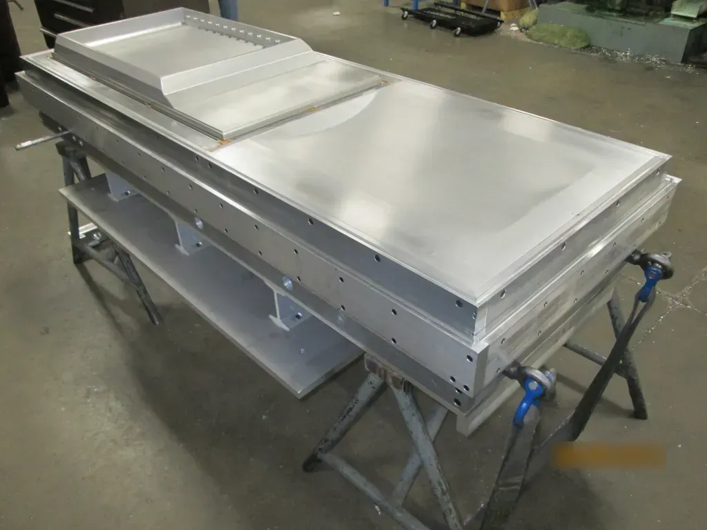 Large silver industrial metal table with a raised panel, on folding stands in a workshop.