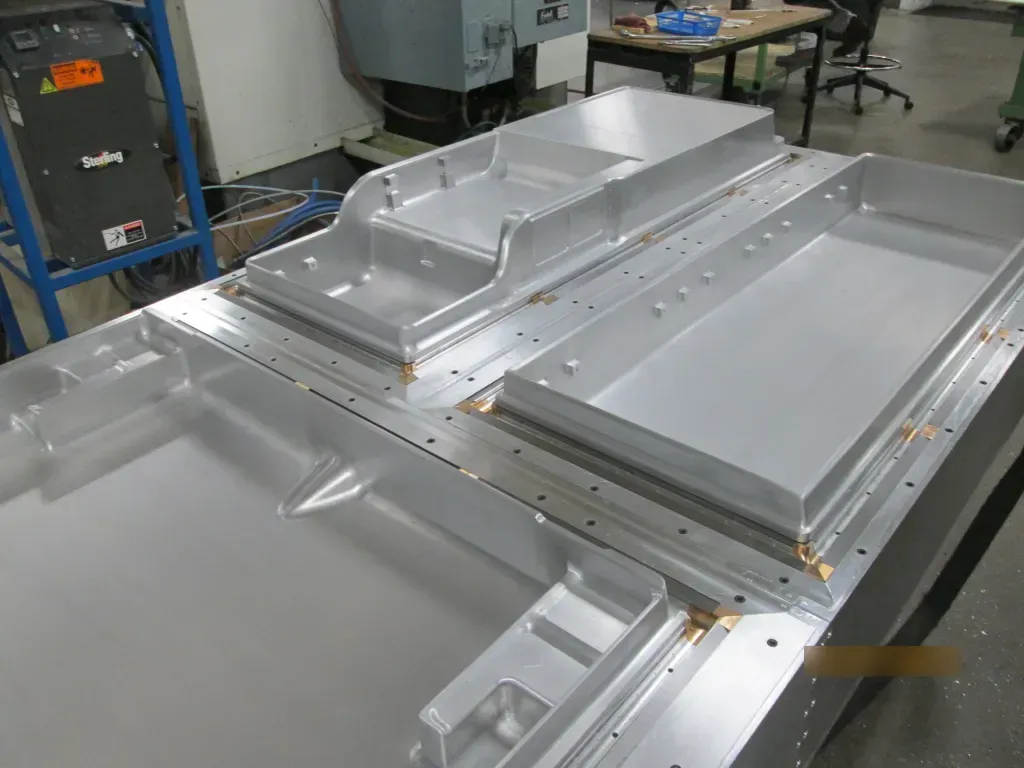 Metal HVAC ductwork panels in a workshop, with silver sheet-metal sections assembled on a worktable.