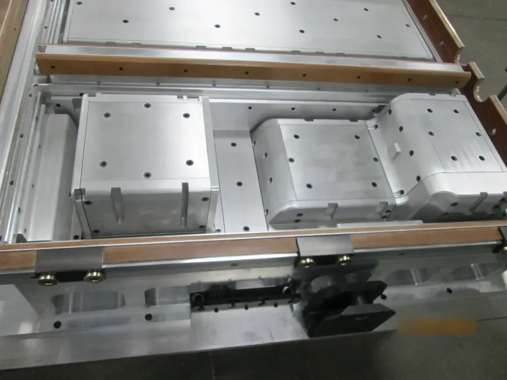 Industrial machinery with three metal blocks inside a rectangular frame, viewed from above