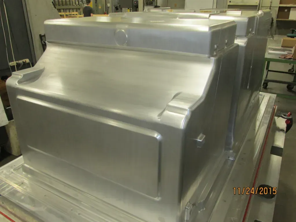 Large silver industrial machine or metal enclosure on a factory floor wrapped in protective plastic.