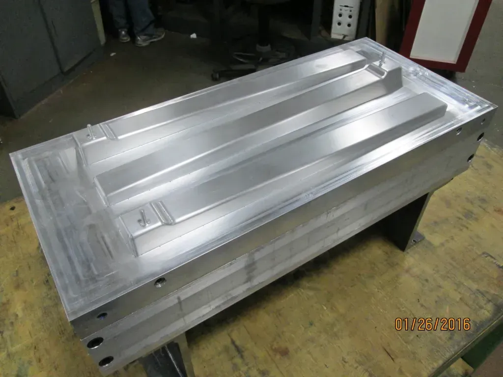 Silver metal industrial mold on a workshop floor, viewed at an angle.