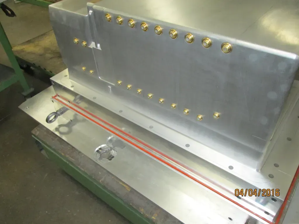 Metal industrial machine component with brass fittings and orange cables on a workbench
