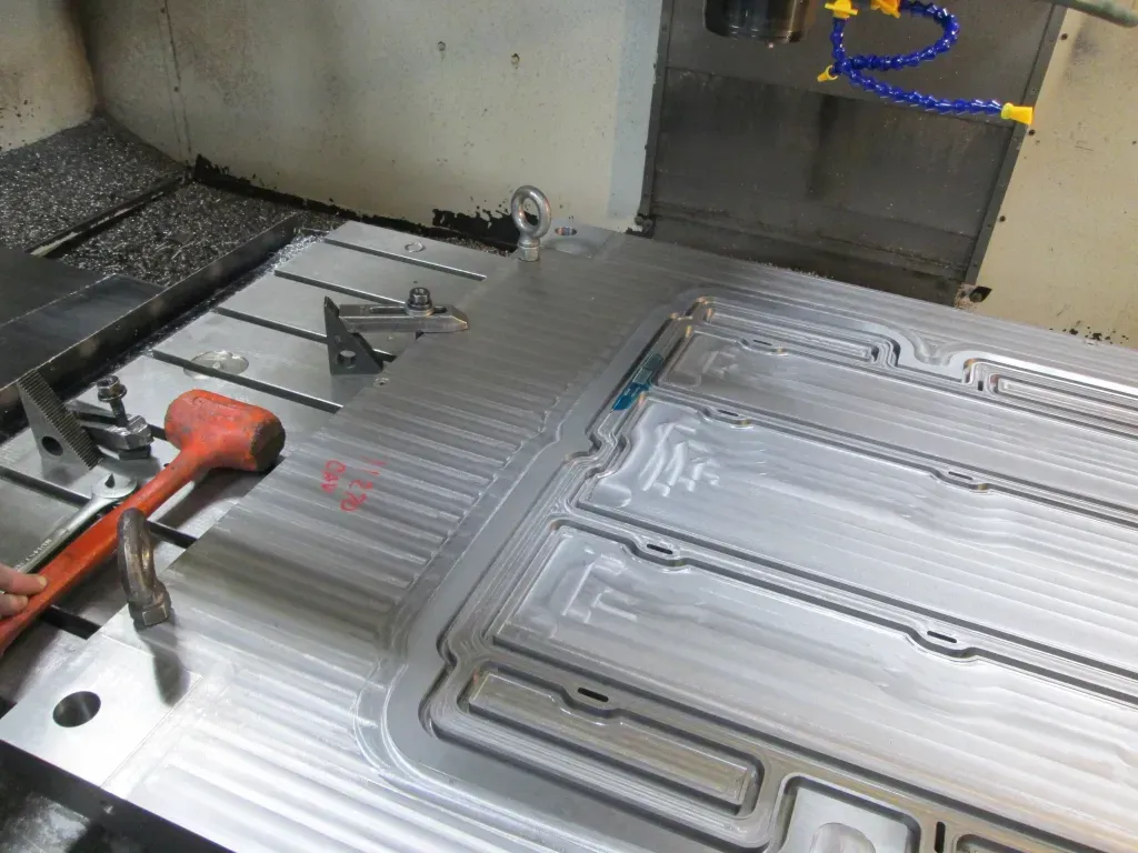 CNC machine milling a metal plate with channels; tools and coolant hoses visible.