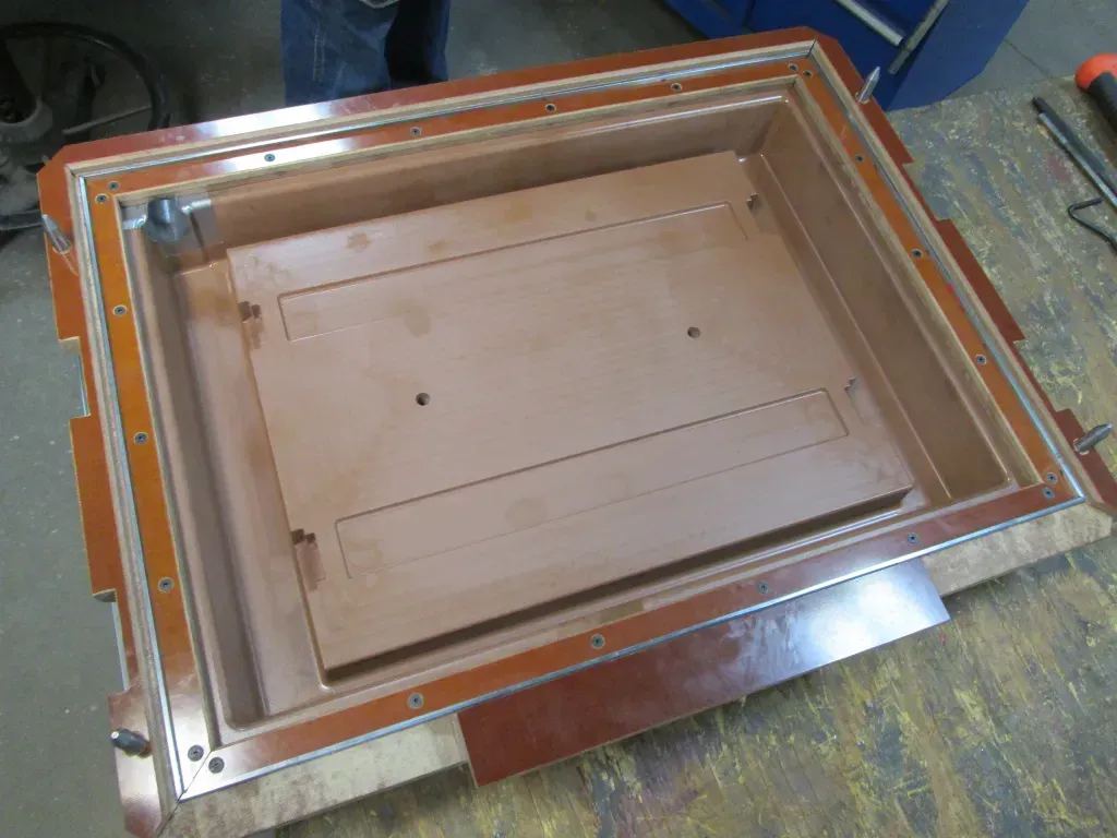Open copper-colored metal frame with a recessed tan panel on a workshop floor