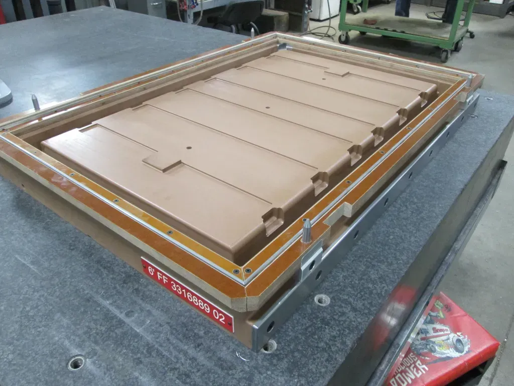 Tan cardboard insert in a wooden frame on a metal worktable in a factory setting