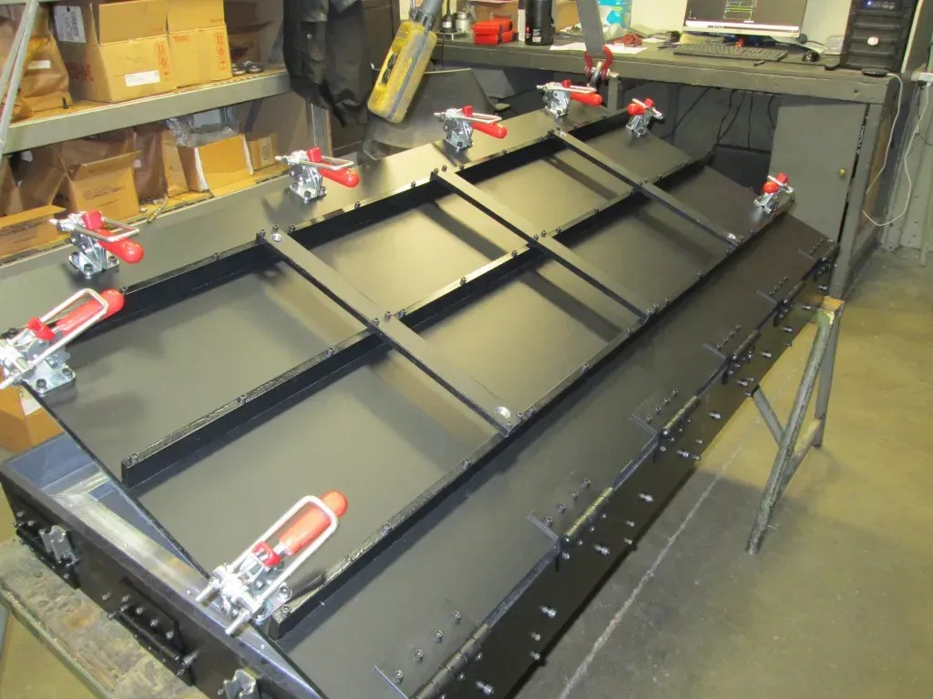 Large black metal frame with red clamps in a workshop, viewed from above
