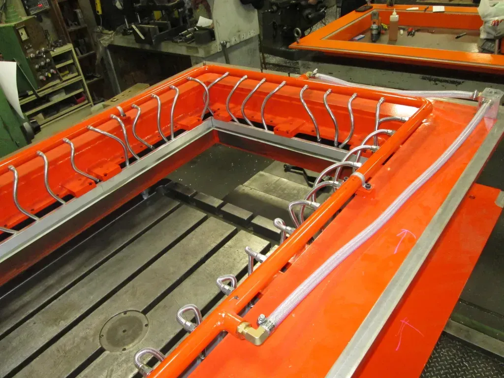 Orange industrial machine frame with coiled hoses and metal rails in a factory setting