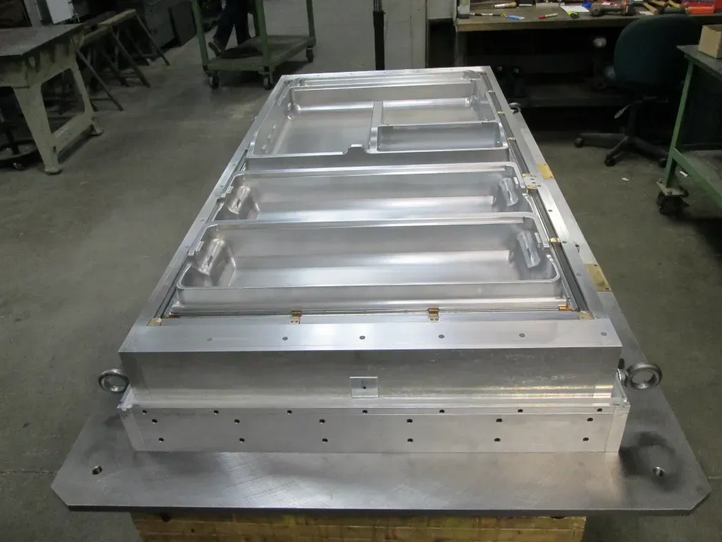Large metal industrial fixture on a workbench in a workshop, with bolts and machined panels.