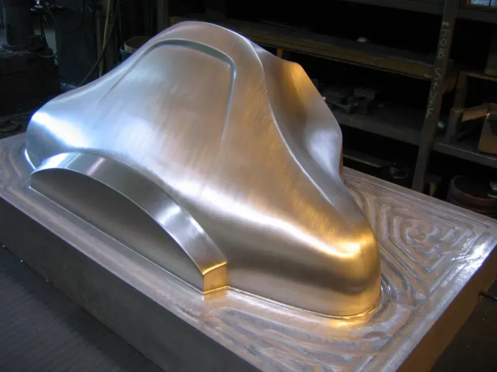 Machined metal sculpture with smooth silver contours on a patterned base in a workshop.