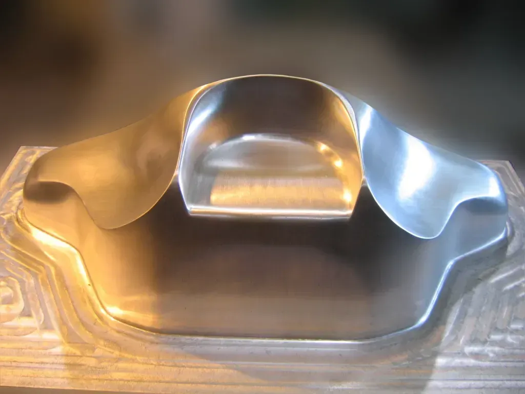 Metallic mold with a wavy, reflective silver surface on a wooden base