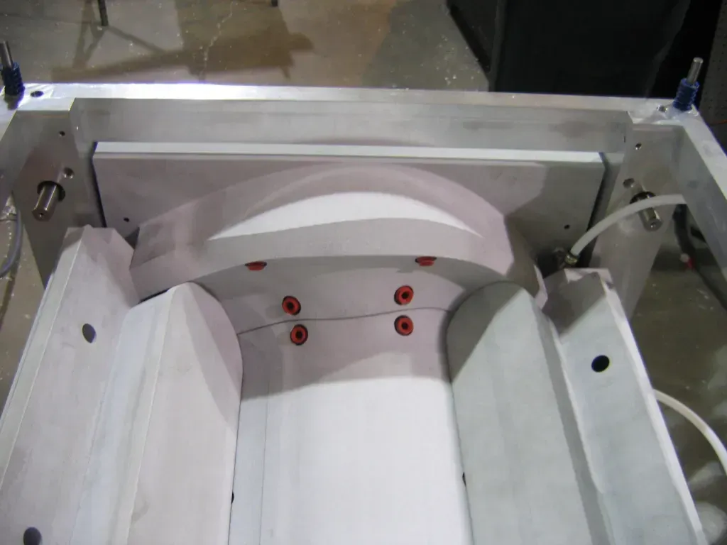 White industrial machine with curved hood and red buttons inside a metal frame