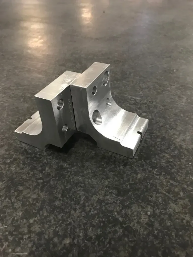 Metal machined bracket with curved cutout and mounting holes on a dark tabletop