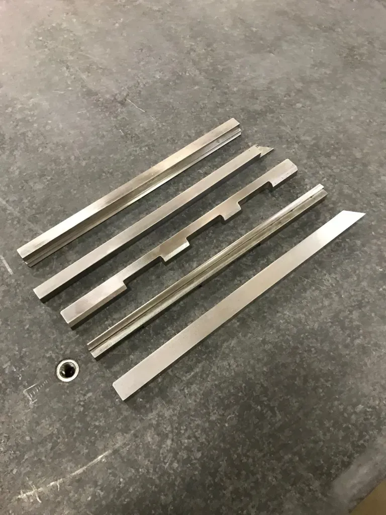 Six silver metal strips and a ring laid diagonally on a dark textured surface.
