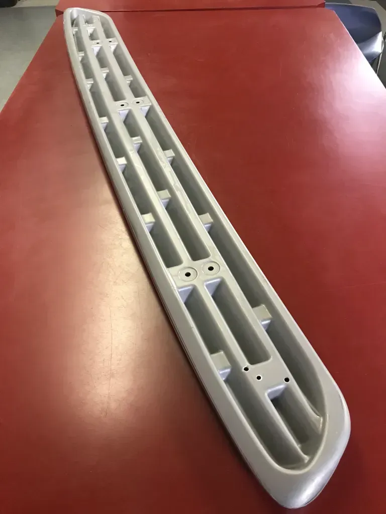 White plastic window blind/air vent piece lying diagonally on a red tabletop.