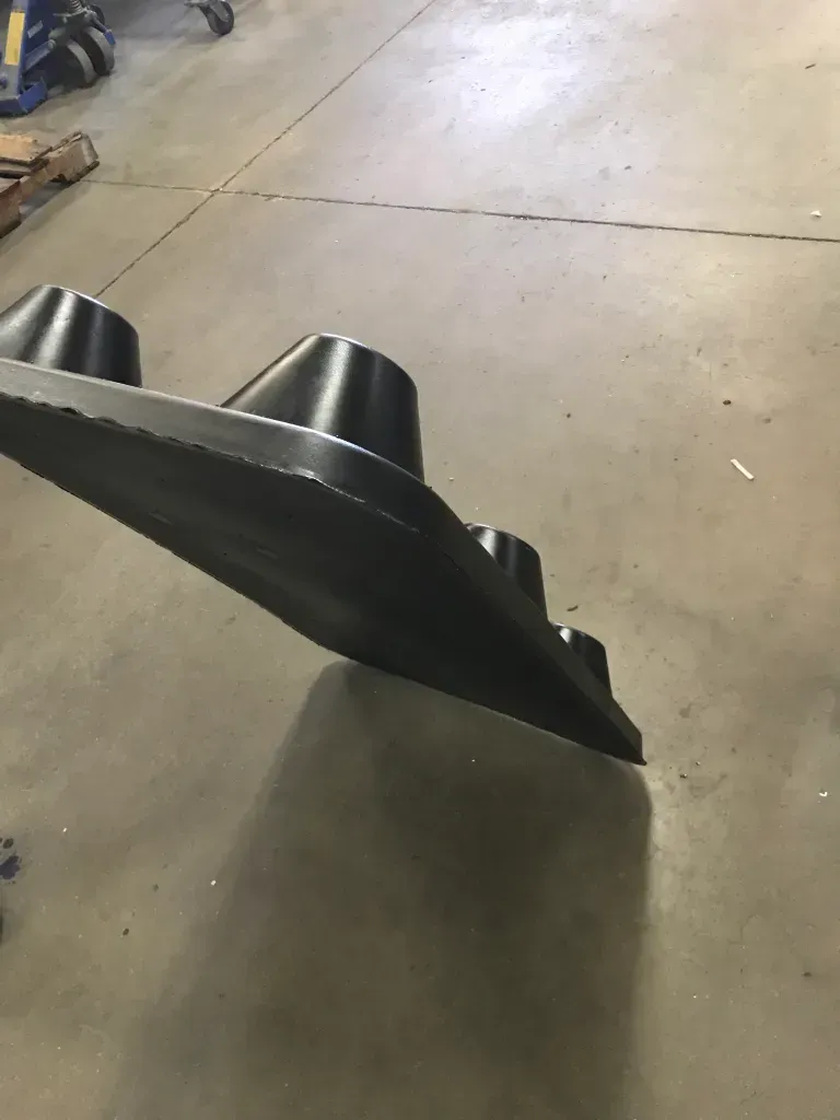 Black metal bucket attachment resting on a concrete floor in a workshop