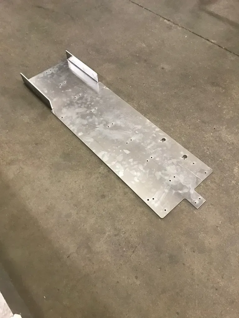 Silver metal ramp plate on concrete floor with raised lip and bolt holes
