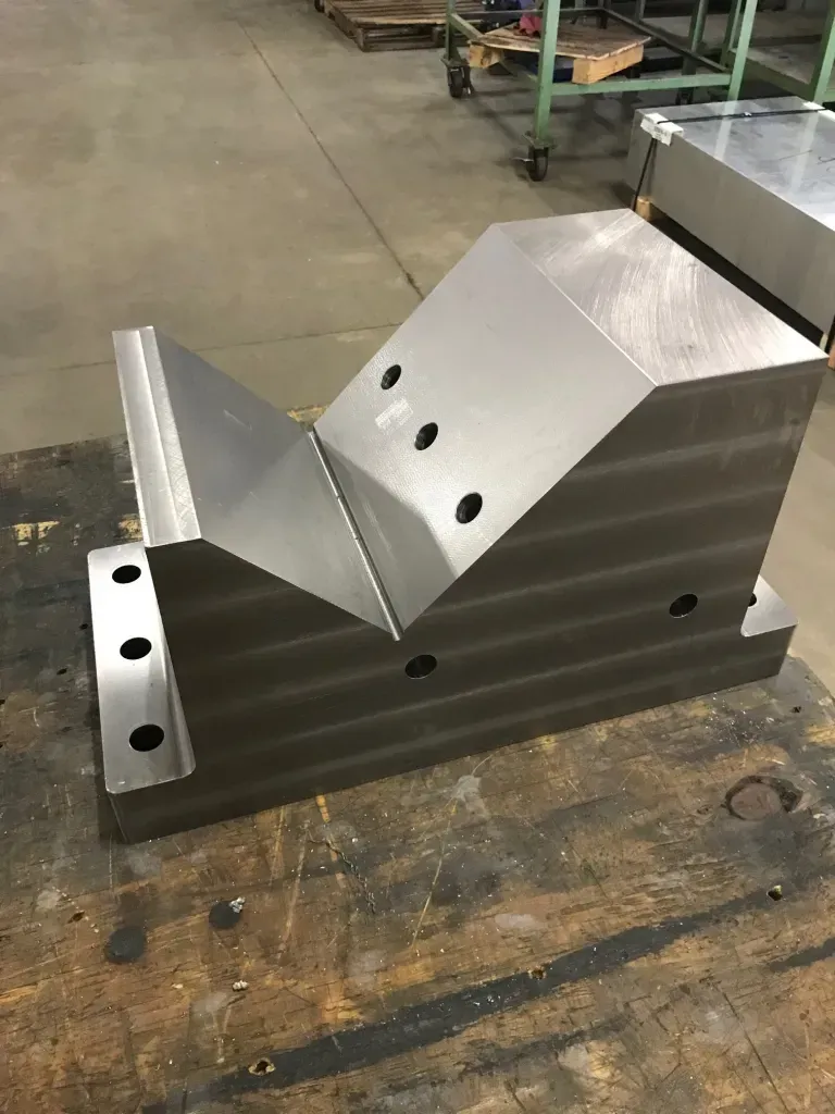 Metal machined part with angled surfaces and drilled holes on a workshop table