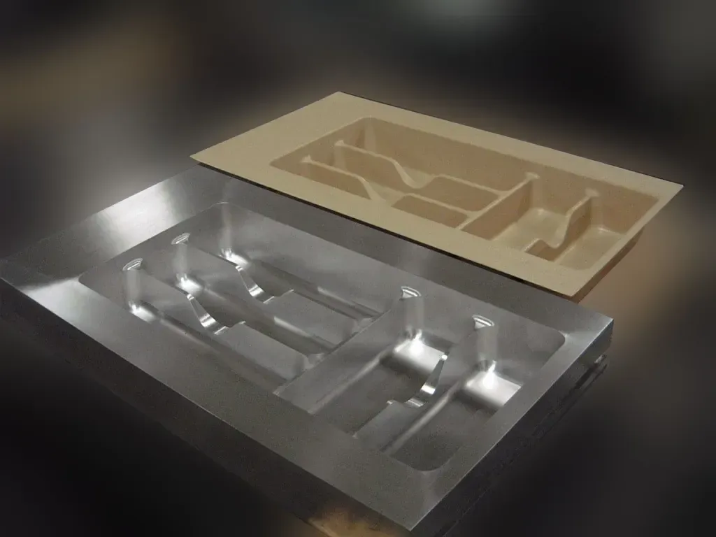 Metal and beige molded trays with carved compartments resting on a dark table.
