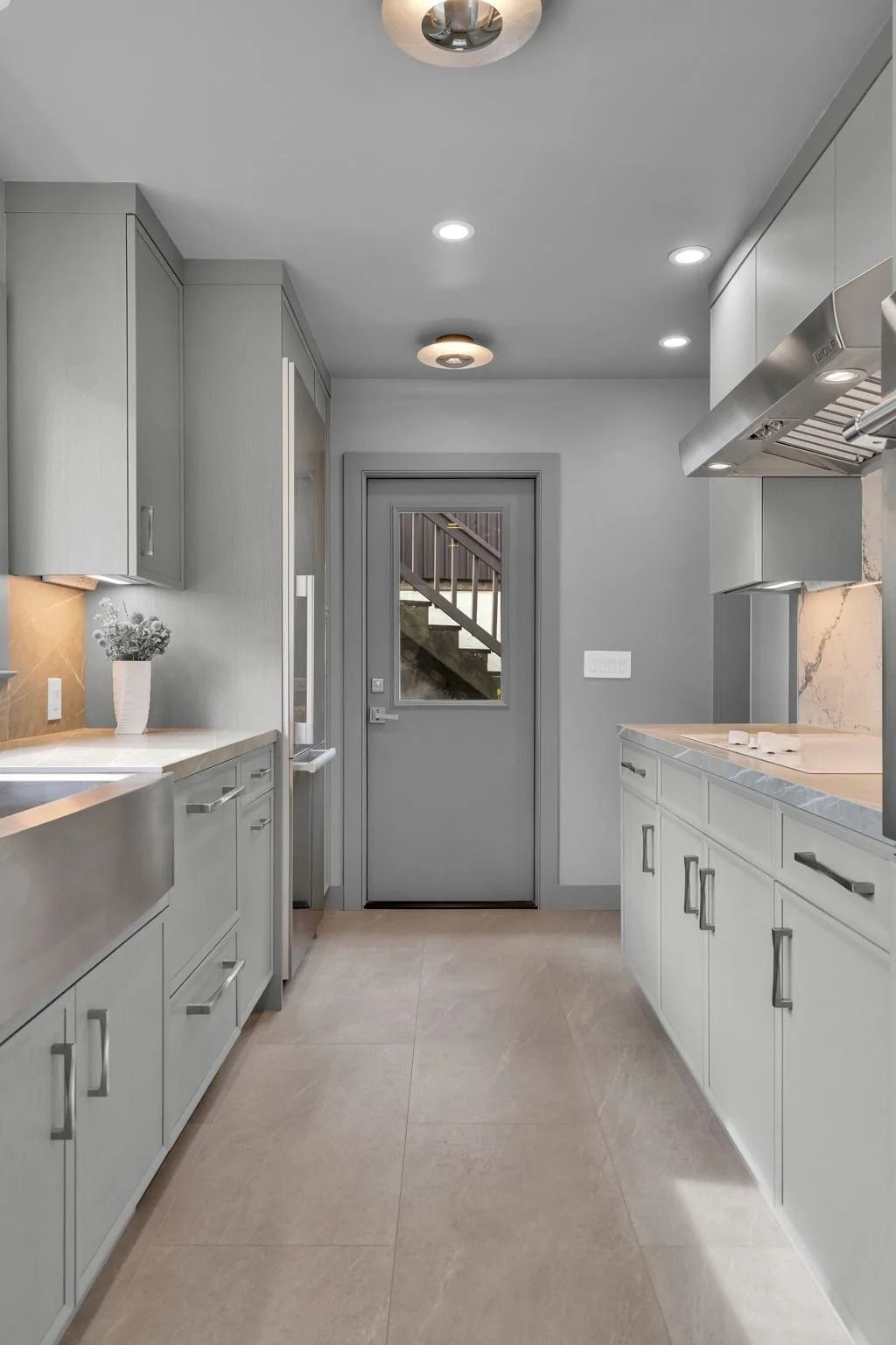 Gray galley kitchen with cabinets, stainless steel sink, and a door leading to stairs.