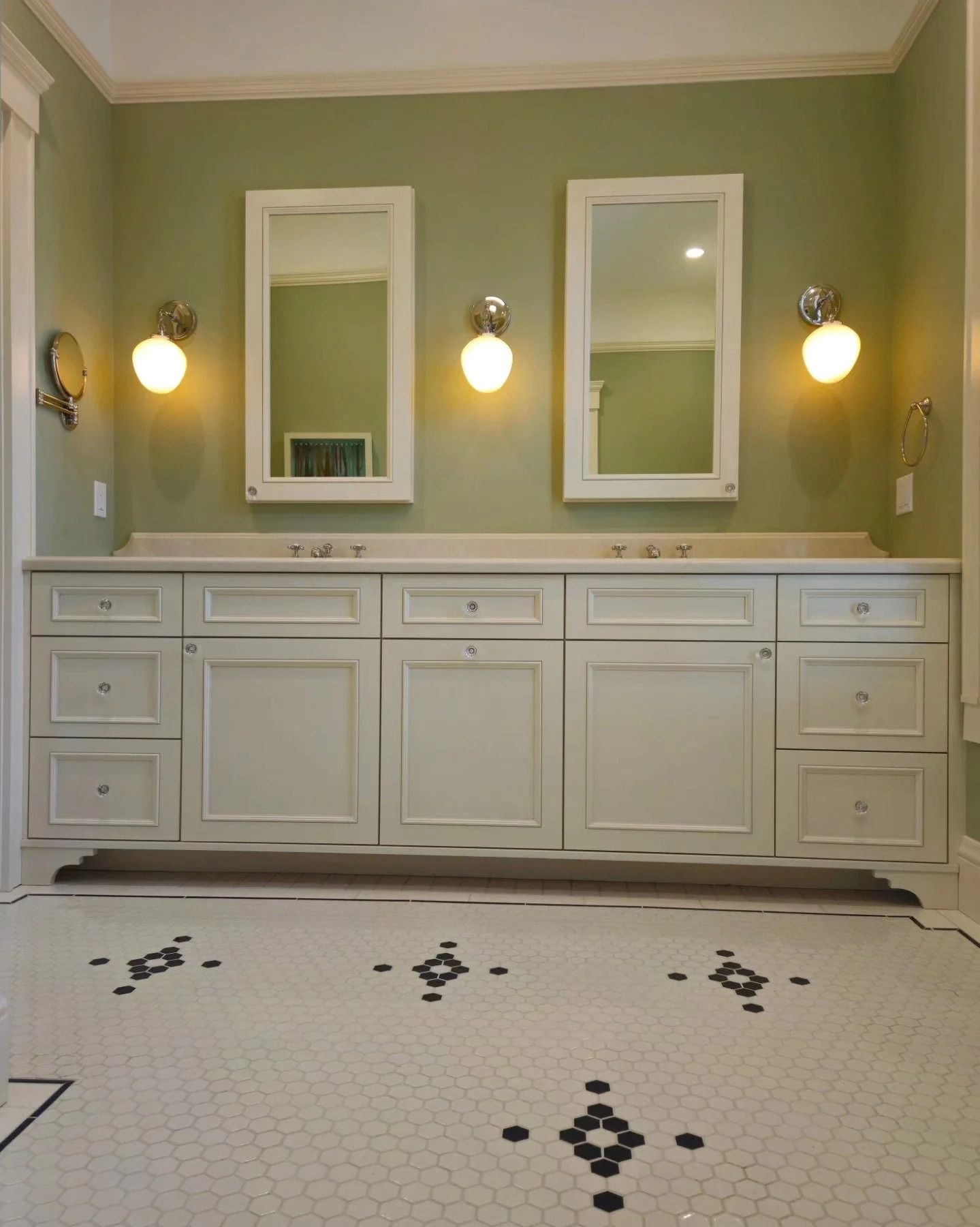 Bathroom with white cabinetry, mirrors, sconces, green wall, and patterned floor.