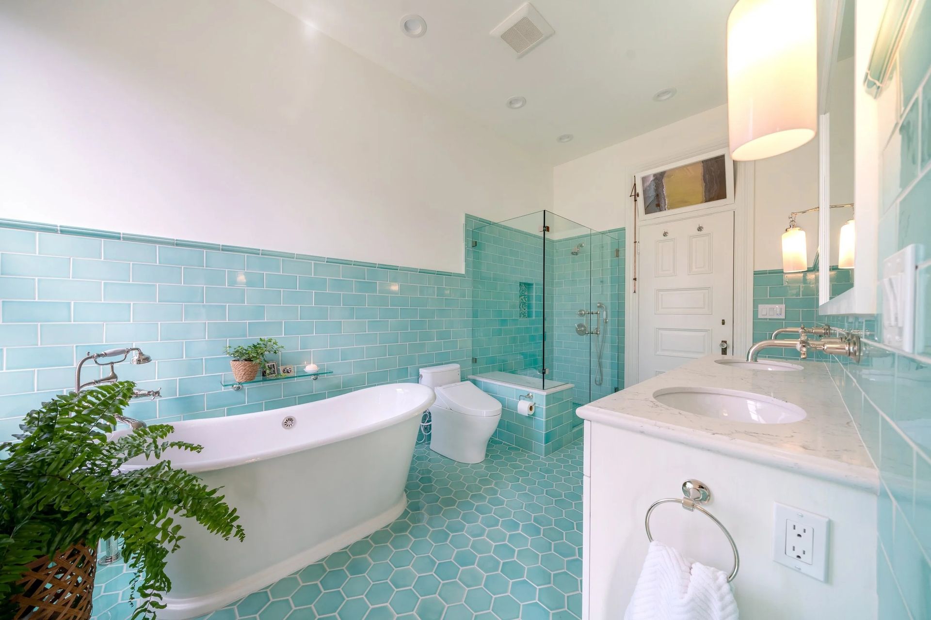 Bathroom with turquoise tiled walls and floor, a white tub, and a glass shower door.