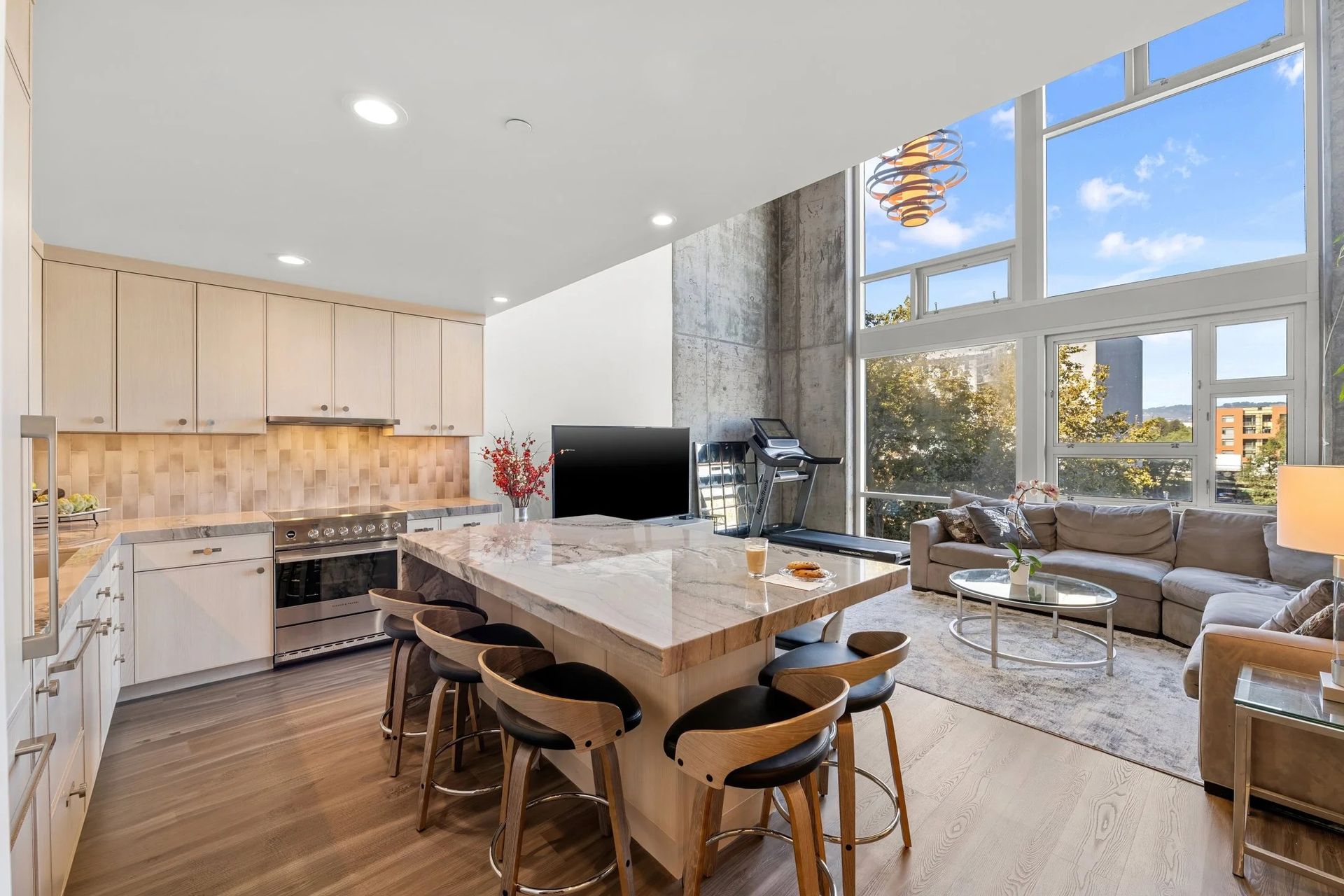 Open-plan kitchen/living room with large windows, island with stools, and treadmill.