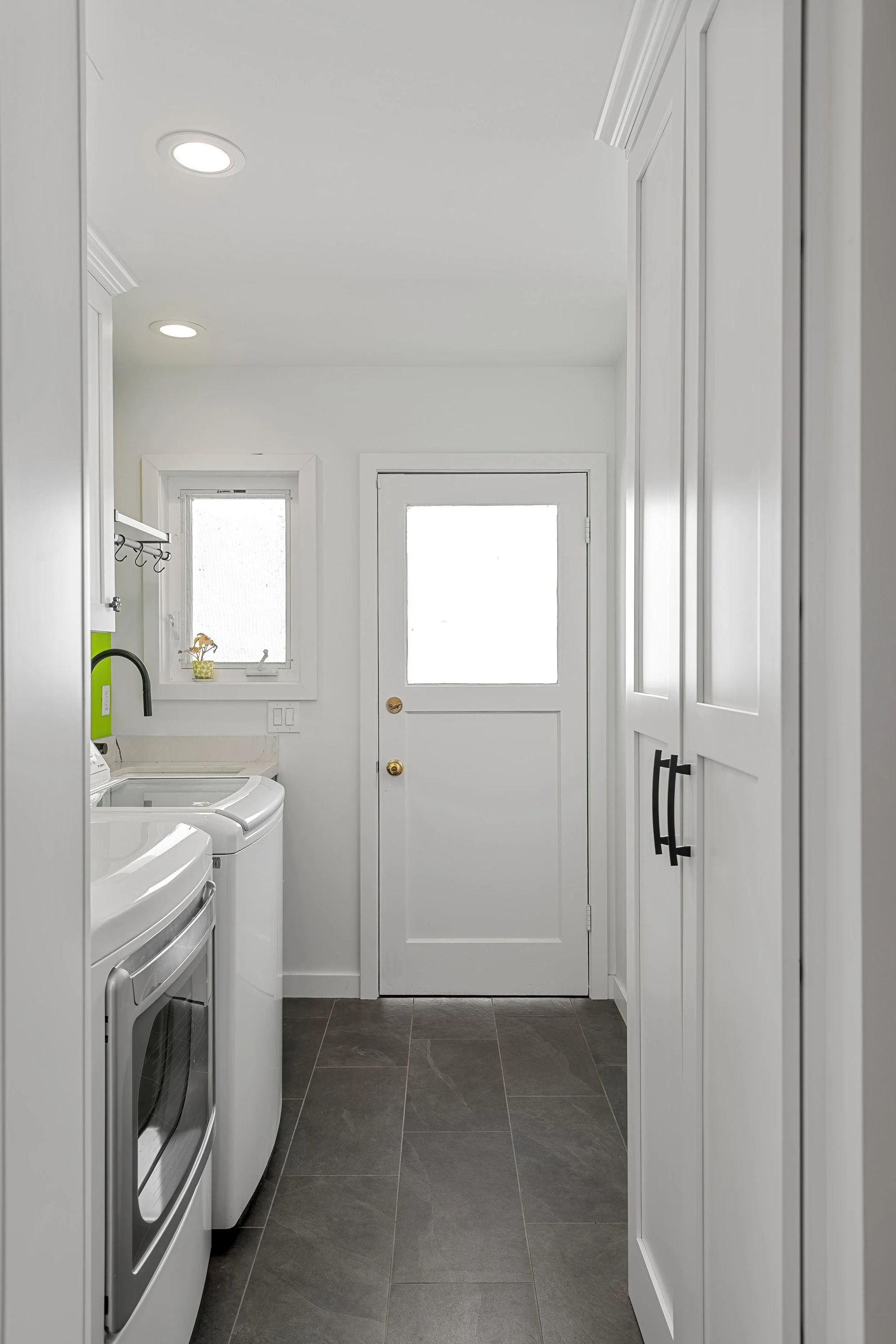 White laundry room with appliances, cabinets, and a door to the outside. Dark gray floor.