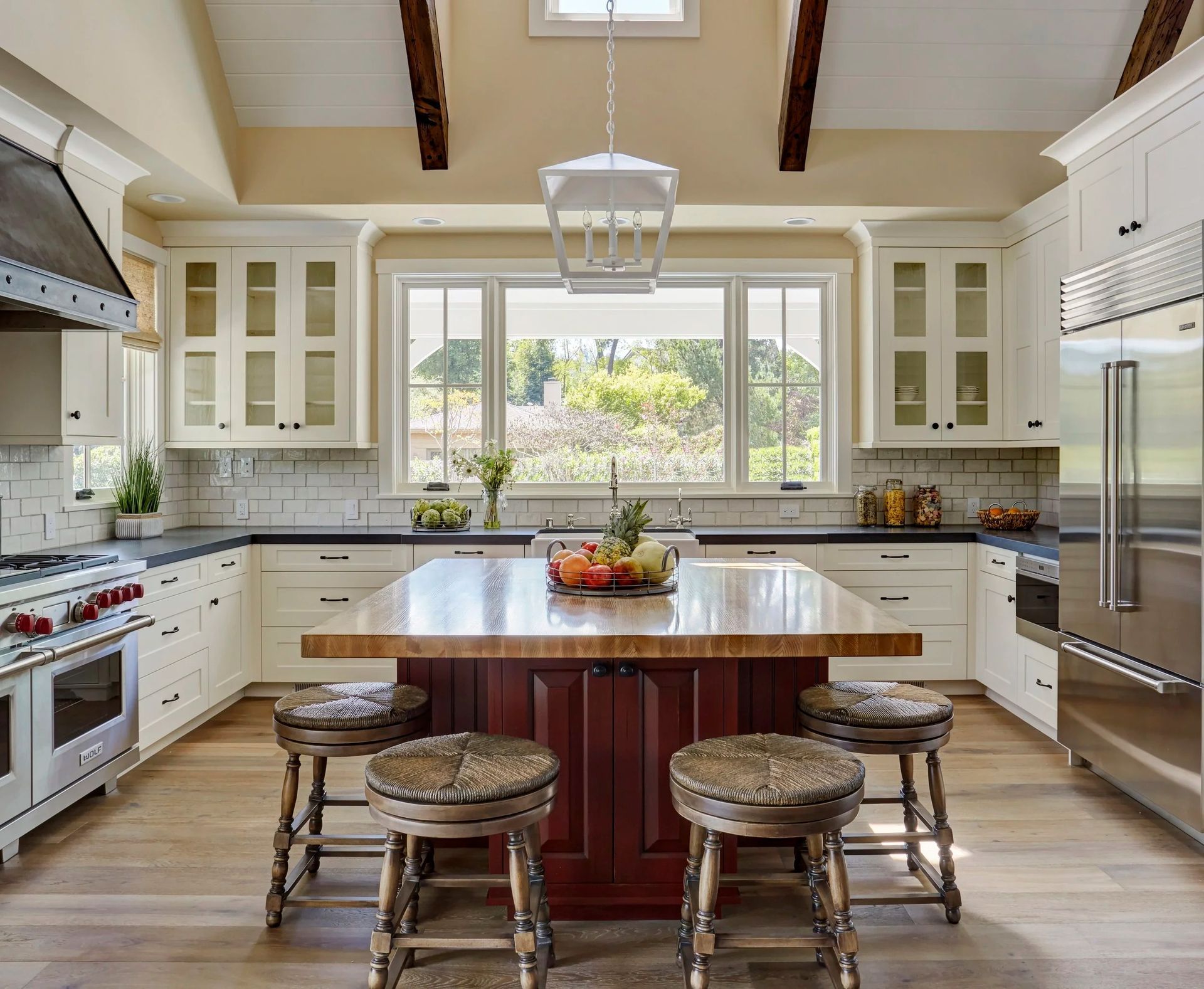 Spacious, bright kitchen with white cabinets, dark countertops, and a red island with wood countertop.