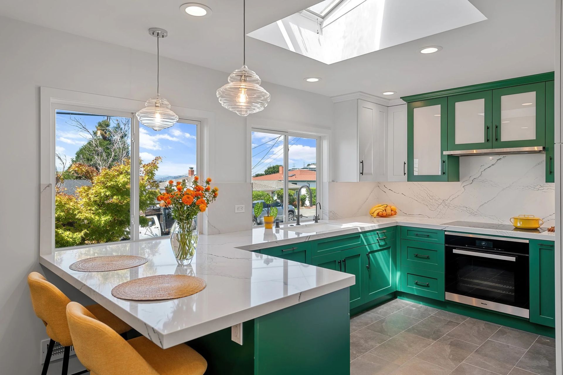 Modern kitchen with green cabinets, white countertops, and bar seating.