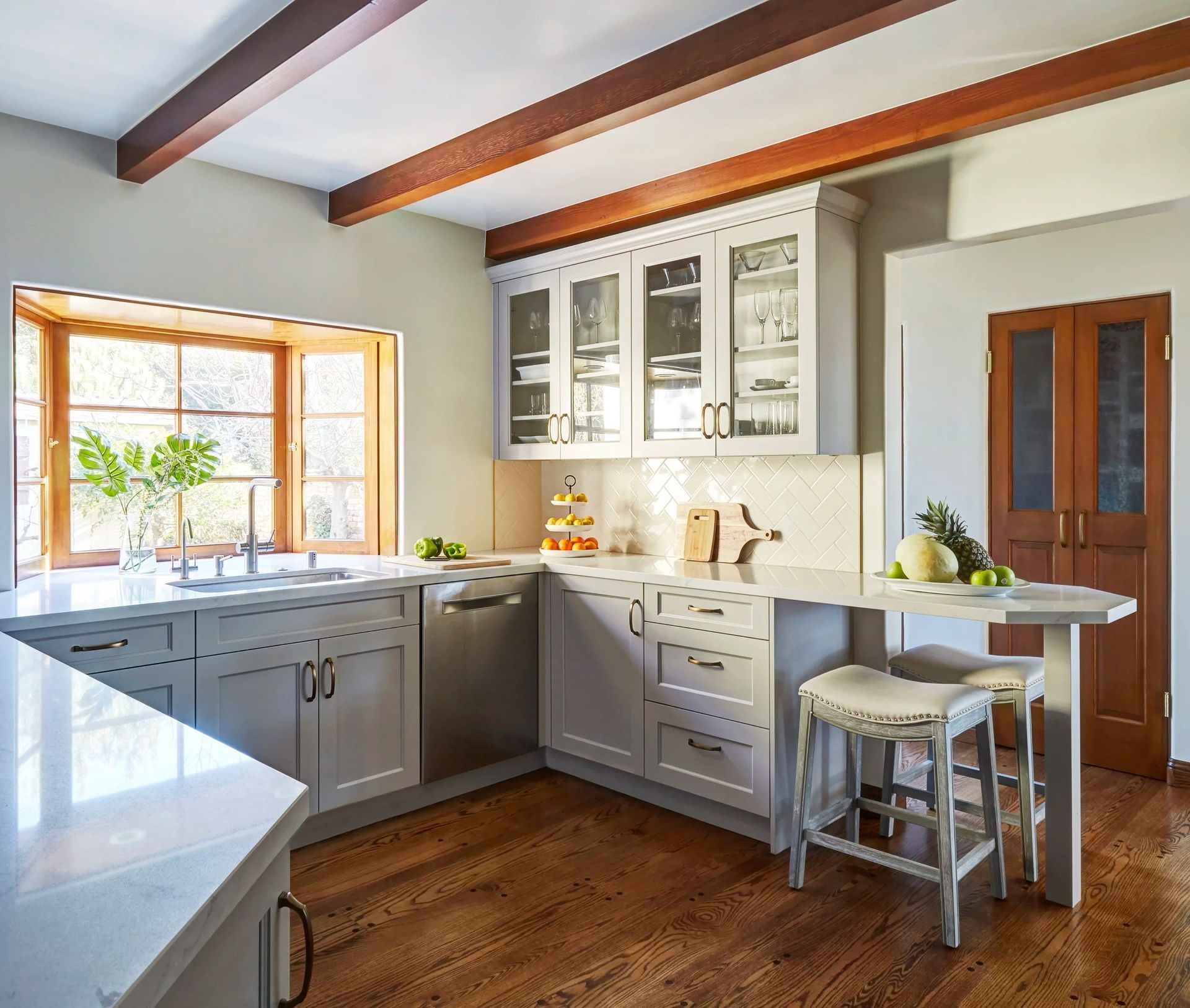 Kitchen with wood beams, light gray cabinets, a window, and a breakfast bar.