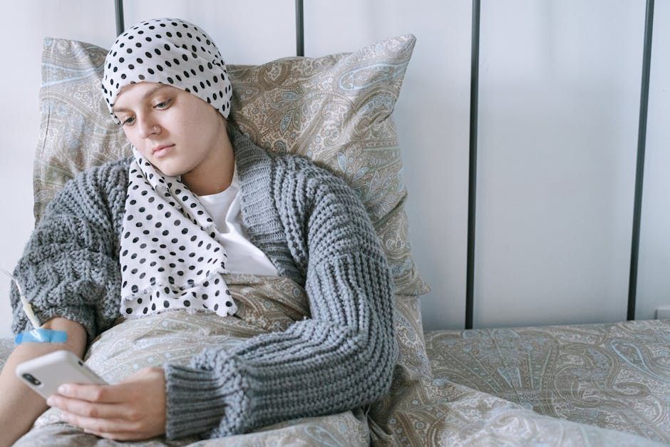A woman with cancer is laying in bed using a tablet.