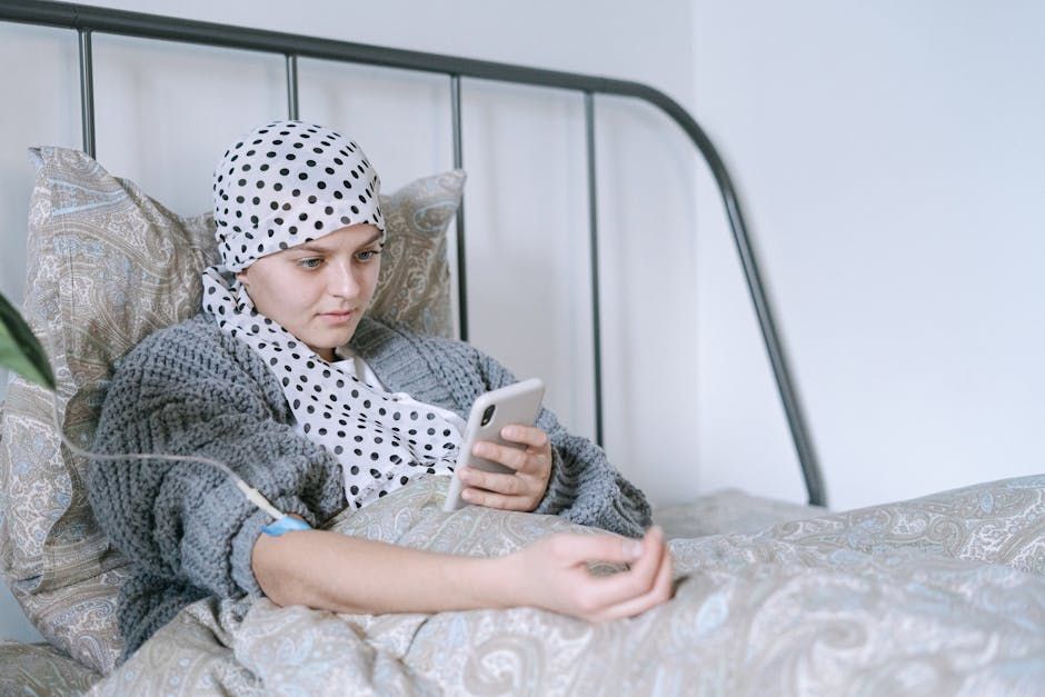 A woman with cancer is laying in bed looking at her cell phone.
