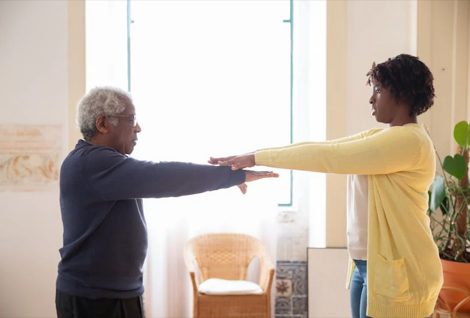 A man and a woman are stretching their arms in a living room.