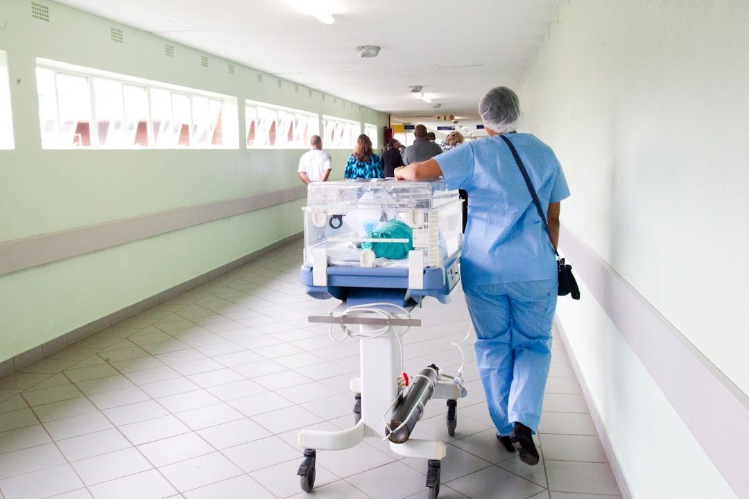 A nurse is pushing a cart with a baby in it down a hospital hallway.