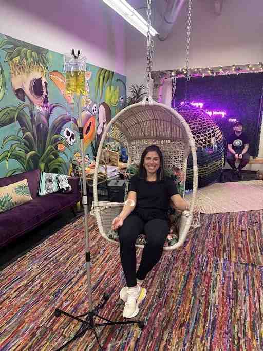 A woman is sitting in a hanging chair with an iv in her hand.
