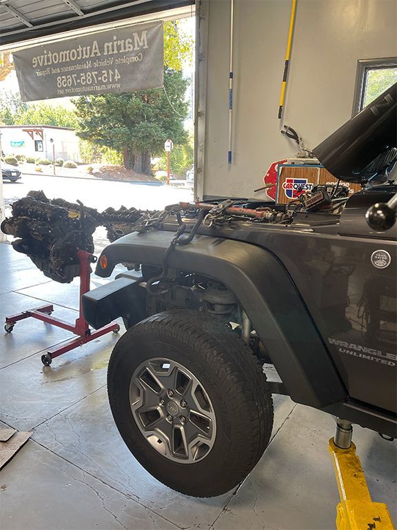 Black Jeep on a lift inside an auto repair shop with its hood open and a mechanic nearby | Marin Automotive