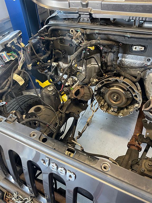 Open Jeep engine bay with transmission removed, showing exposed mechanical parts and wiring. | Marin Automotive