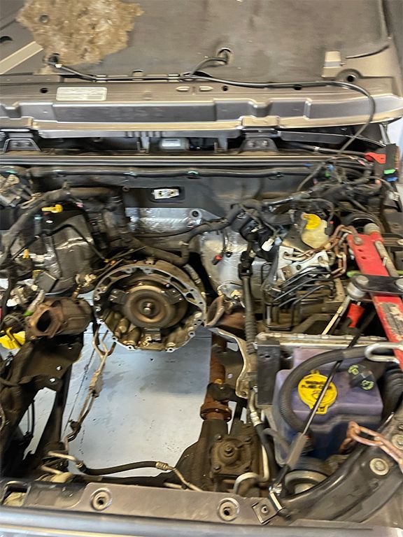 Car engine bay with the engine removed, exposing the transmission, hoses, and wiring. | Marin Automotive