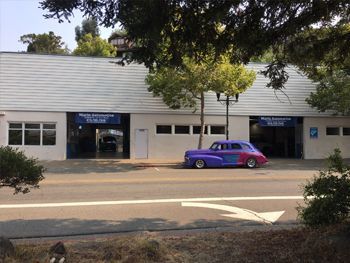 Single-story storefronts with a purple car parked outside along a street | Marin Automotive