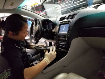 Person cleaning the dashboard and center console of a car interior with a cloth and bottle | Marin Automotive
