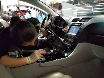 Child leaning into a car interior near the dashboard and steering wheel, with a lit center display. | Marin Automotive
