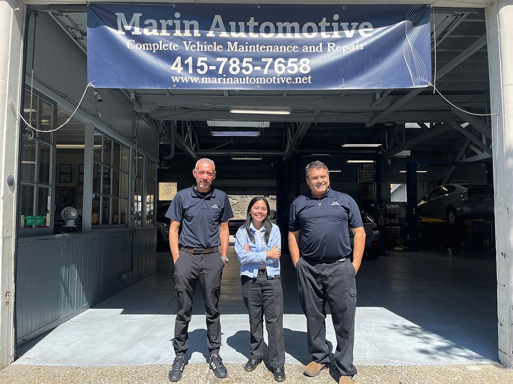 Three mechanics standing in a garage bay under a Marin Automotive sign. | Marin Automotive