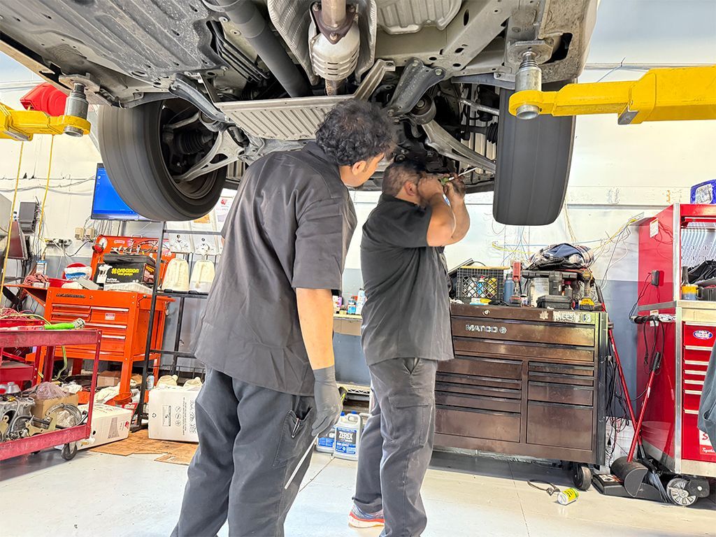 Two mechanics inspecting a car’s underside in an auto repair shop with tools and lift equipment nearby | Marin Automotive