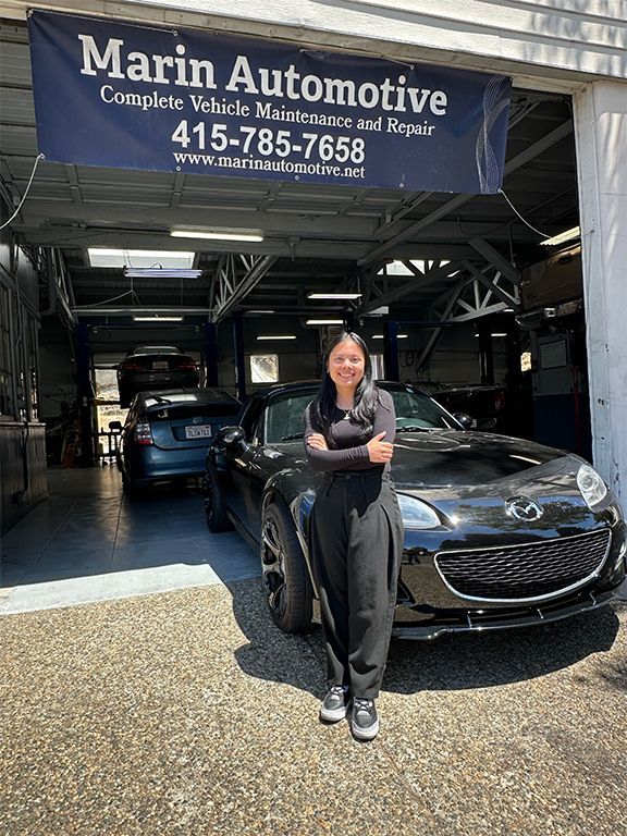 Woman standing by a black car at Marin Automotive service garage entrance. | Marin Automotive