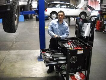 Mechanic in a blue shirt stands beside an automotive diagnostic machine in a garage with cars on lifts. | Marin Automotive
