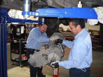 Two mechanics in blue shirts inspecting a car engine under a lift in a garage | Marin Automotive