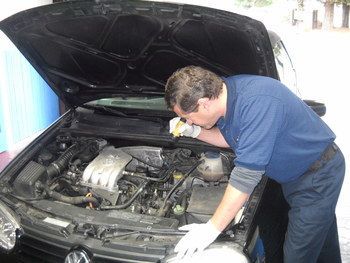 Mechanic inspecting a car engine with the hood open, wearing gloves in a garage | Marin Automotive