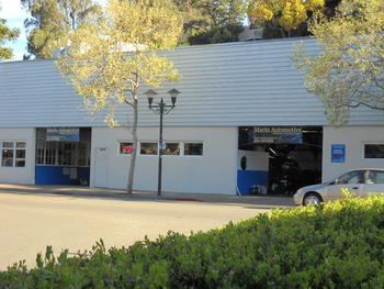 White building with blue garage doors and parked car beside a streetlamp, partially obscured by trees and shrubs