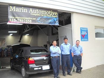Three men stand outside Marin Automotive garage beside a black car. | Marin Automotive