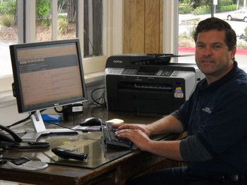 Person working at a desk with a computer and printer in an office setting | Marin Automotive